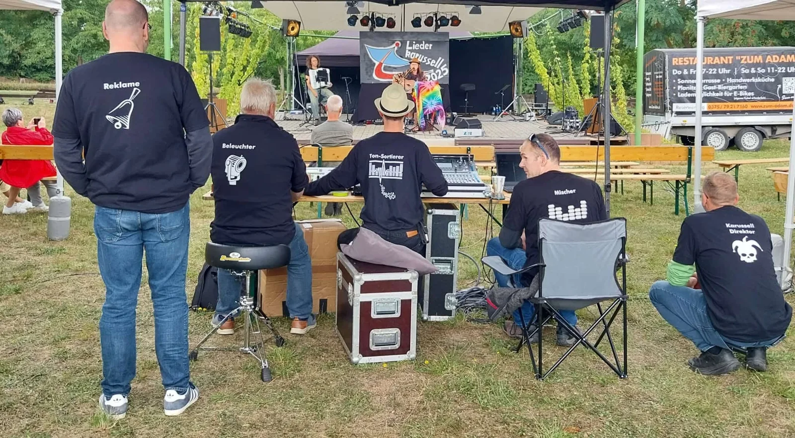 Fünf Helfer in beschrifteten Shirts vor der Bühne, an Mischpult und Licht