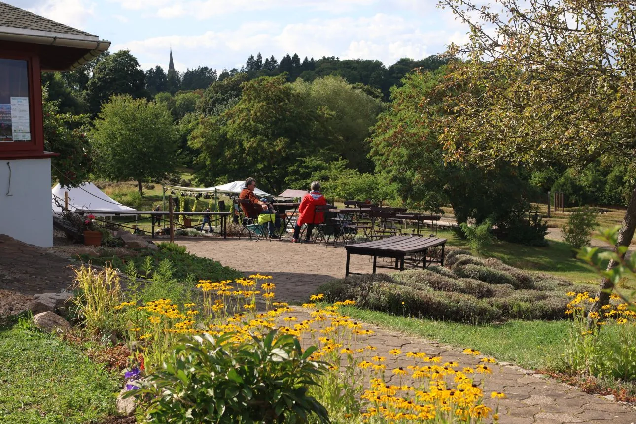 Weg durch den Erlebnisgarten mit blühenden Beeten, im Hintergrund die Zelte des Festivals