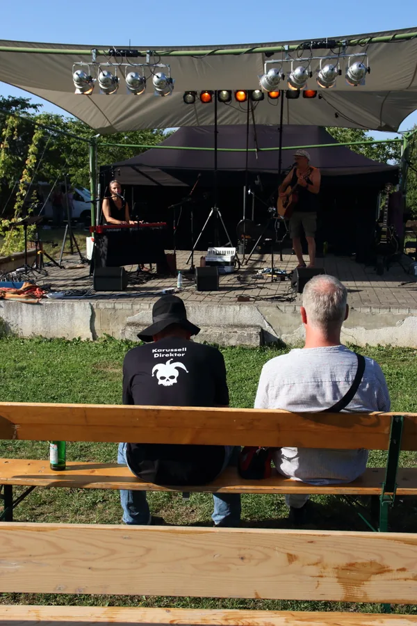 Zwei Gäste sitzen auf einer Bierzeltgarnitur und schauen zur Bühne